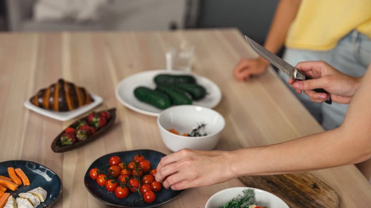Mains disposant des légumes et des tomates dans des plats, sur une table en bois