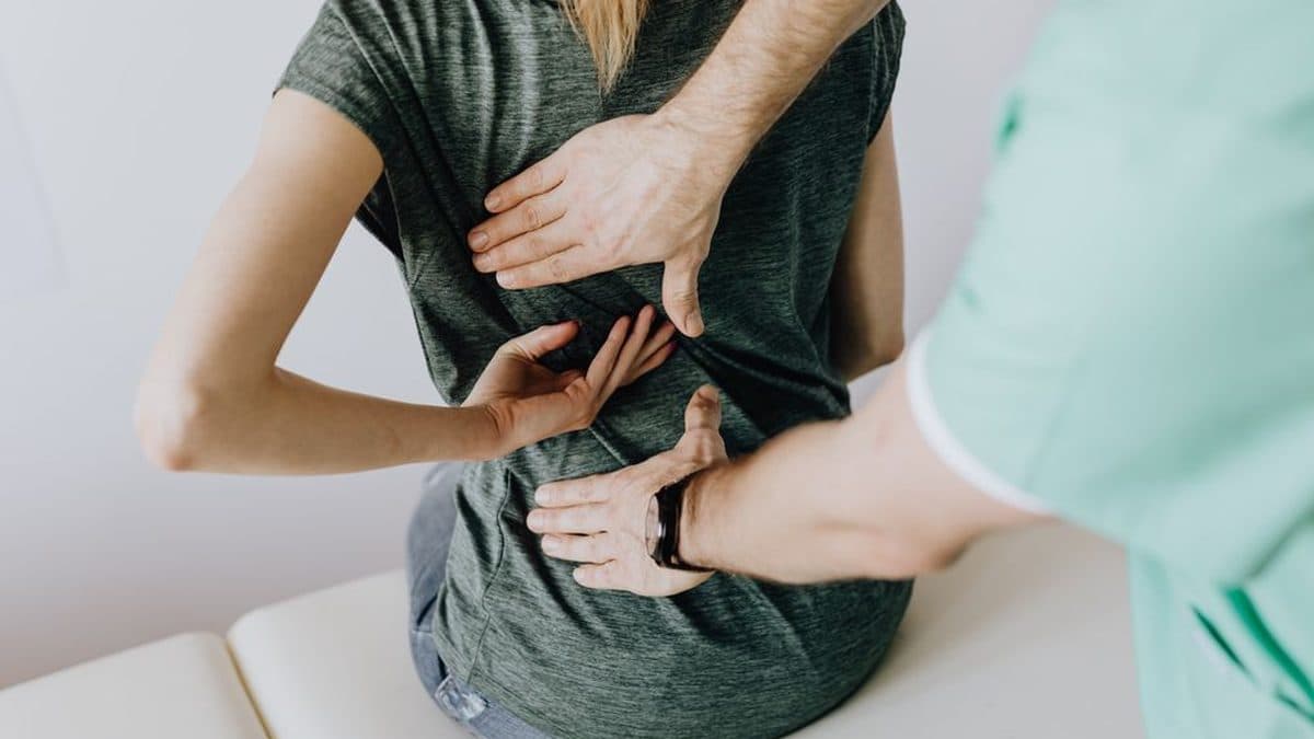 Mains d'une physiothérapeute palpant le bas du dos d'un patient debout