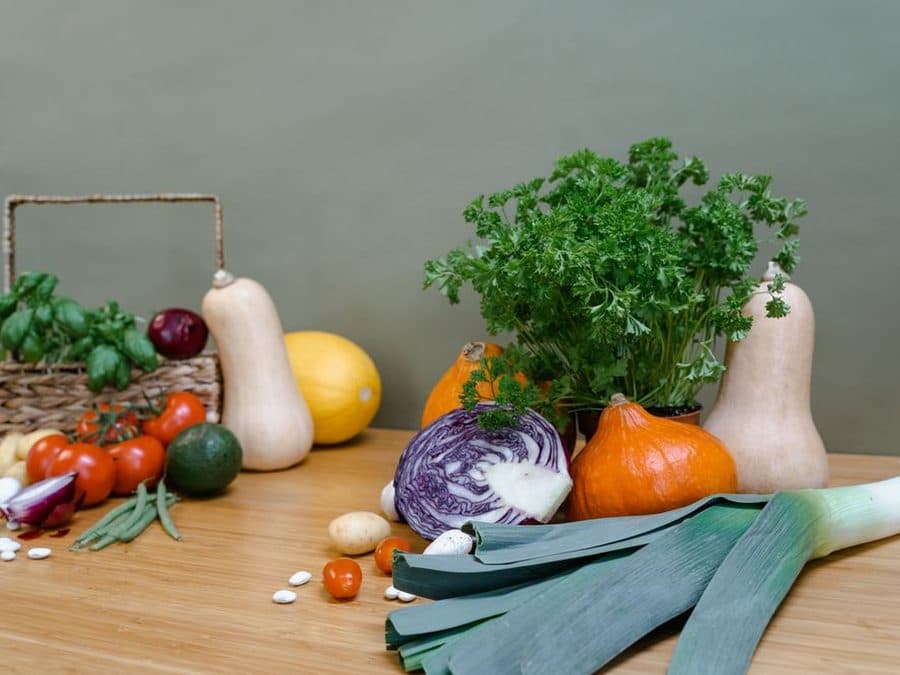 Légumes frais de saison — courges, poireaux, tomates, herbes — posés sur une table en bois