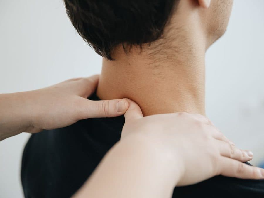 Mains d'une physiothérapeute travaillant la nuque et le trapèze d'un patient